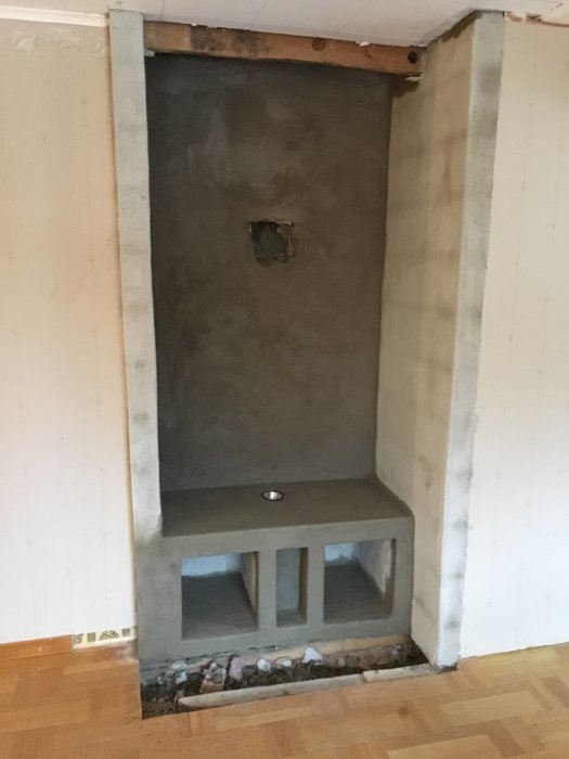 Nybyggd och putsad öppen spis-liknande struktur med hylla för ved, innan installation av kamin.