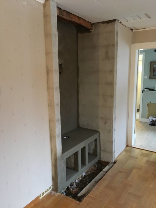 En hörna av ett vardagsrum under renovering med nybyggda betongstödväggar och en upphöjd plattform i förberedelse för installation av en kamin.