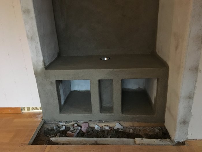 Pågående installation av en murad kaminbänk med öppen spis och vedförvaringsutrymme i ett renoveringsprojekt för ett hem.