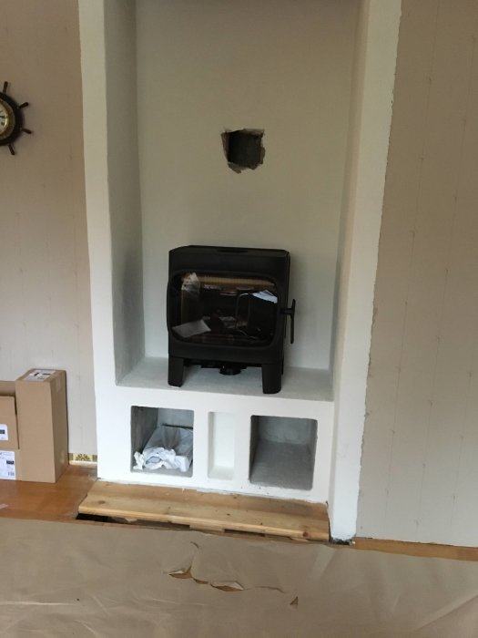 Svart Jøtul F305 kamin på podiest i nybyggt murat värmeelement i ett vardagsrum under renovering.