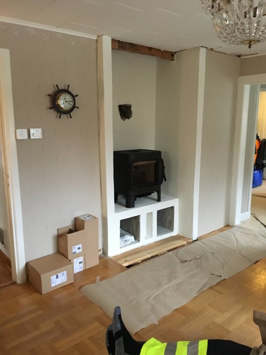 Nyinstallerad svart Jøtul F305 kamin på vitmålad bärande vägg med plats för ved under och skyddspapp på golvet.