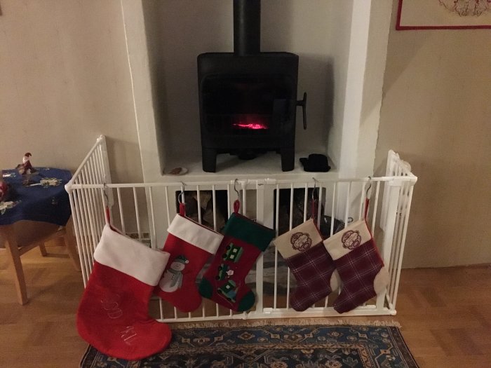 En nyligen installerad svart kamin bakom en vit säkerhetsgrind med julstrumpor hängande på grinden.