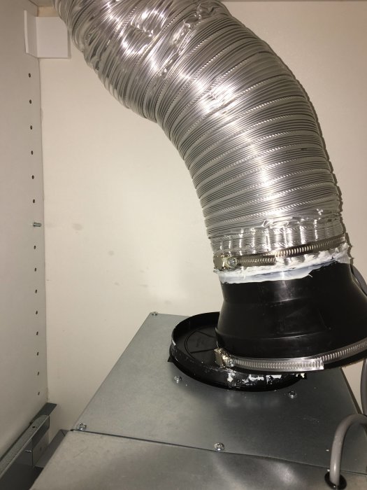 Flexslang för köksfläkt med löst åtdragen slangklämma och ett öppet kallrasskydd utan isolering.