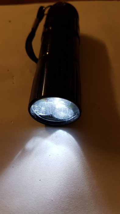 Ficklampa med cirkelformad polariserad lins skapar ljusfläck på underlaget för asbesttest.
