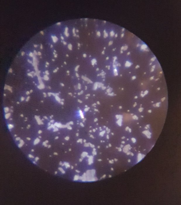 Mikroskopbild av eternitprov med polariserat ljus som visar ljusa och mörka partier, experiment för att identifiera asbest.