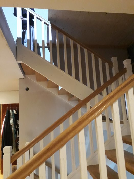 Nymonterad trappa i inomhusmiljö med trästaket och vilplan, delvis skymd av en pelare.