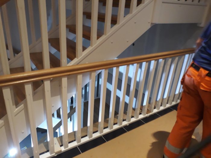Nyinstallerad trätrappa med vita stolpar och handledare i trä, synlig arbetare i arbetskläder.