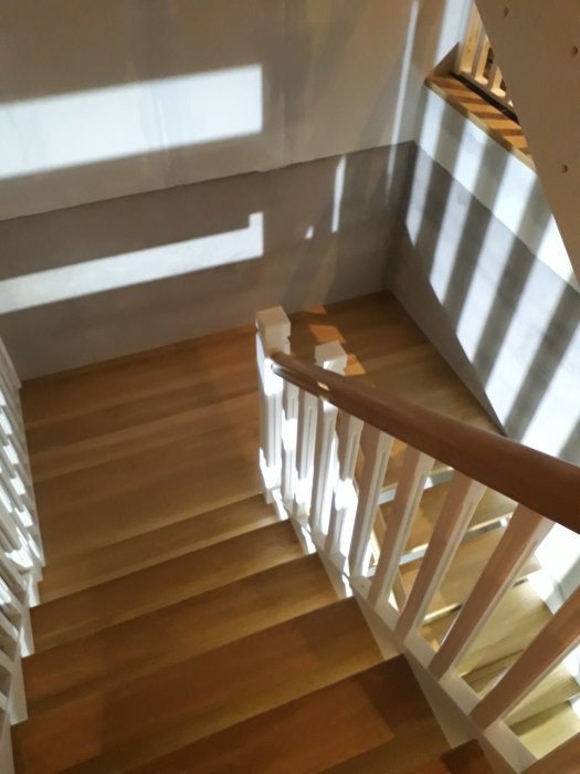 Nyinstallerad trätrappa med vilplan och vitt räcke, i ett hem med solljus som kastar skuggor.