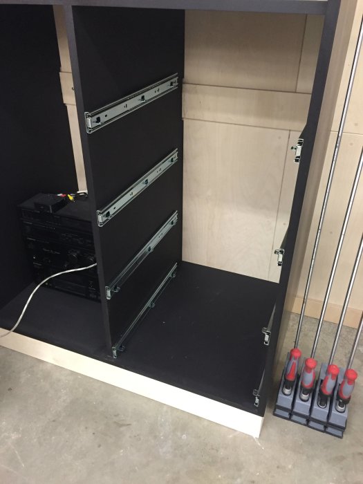 Svart skåpstomme med fyra monterade metallskensbeslag för lådor och en uppsättning skruvmejslar.