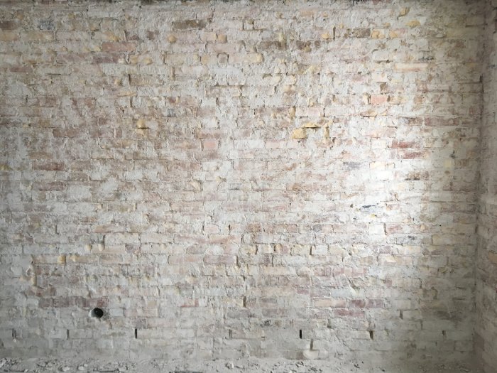 Närbild på en ojämnt putsad tegelvägg med gamla putsrester och sporadiska fläckar av lim eller tapet.