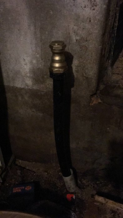 En mörk bild på en stående rörinstallation med en mässingskoppling mot en betongvägg.