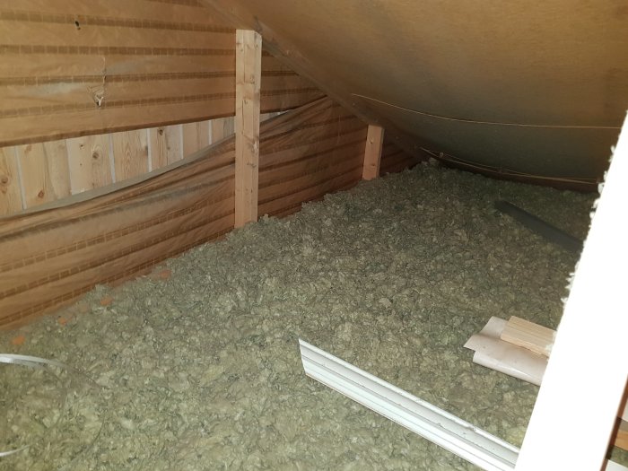 Invändig vy av vind med isolering, träbjälkar och plastfilm mellan tak och isolering.