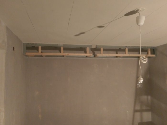 Pågående renovering med synliga träreglar i ett tak där spotlights ska installeras, bredvid en temporär taklampa.