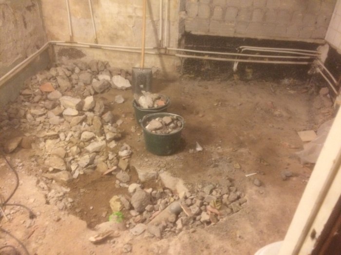 Nedrivet källargolv med bråte och två hinkar, en spade syns i en tom byggnadsyta under renovering.