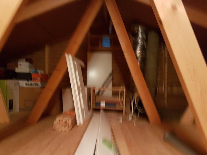 Suddig bild på ett oinrett vindutrymme med synliga takbjälkar och lagrade föremål.