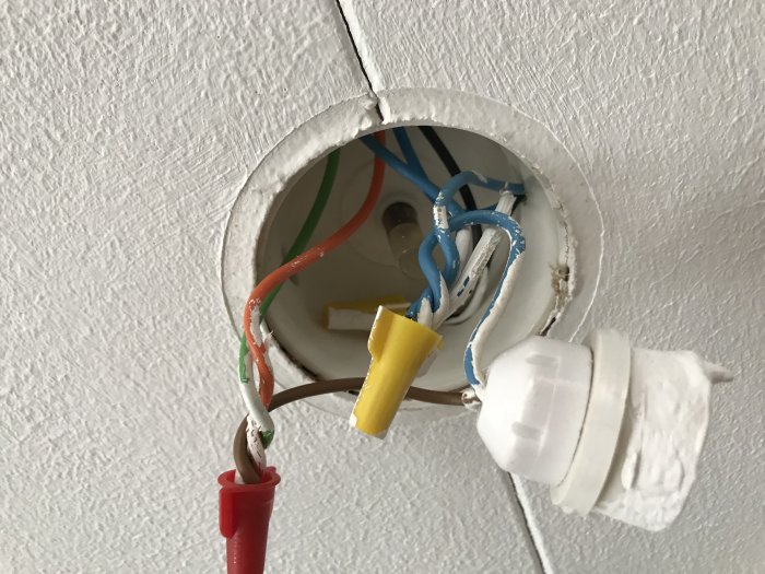 Öppen taklampa med synliga elektriska anslutningar och isoleringstejp.