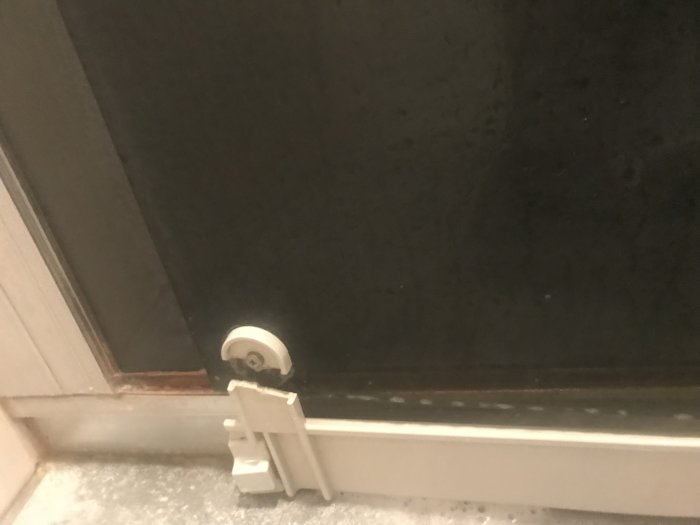 Sprucken plastbit på en skjutdörrs hjulmekanism vid duschen.