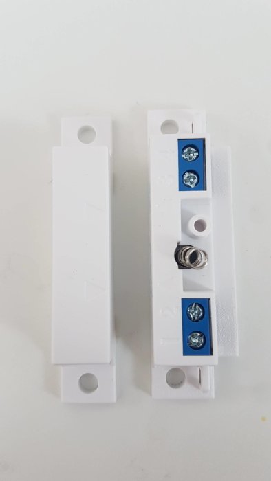 Vita MK440 installationsdelar med pilmarkeringar och ledningsterminaler, monterade sida vid sida.