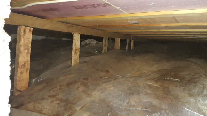 Nyuppsatta trästolpar under bjälklag i källare mot berggrund med plastfolie på marken.