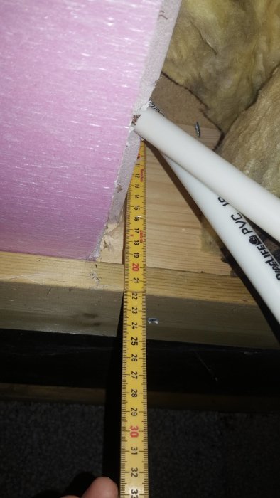 Måttband som visar avståndet mellan träbjälklag och isoleringsmaterial vid byggprojekt.