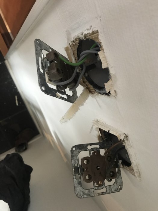 Två öppna eluttag med strömbrytare och synliga ledningar i en vägg.