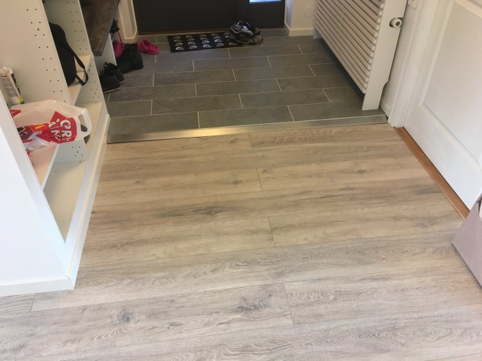 Nyinstallerat laminatgolv med vägglistning, klädhängare och elementskydd i ett entrérum.