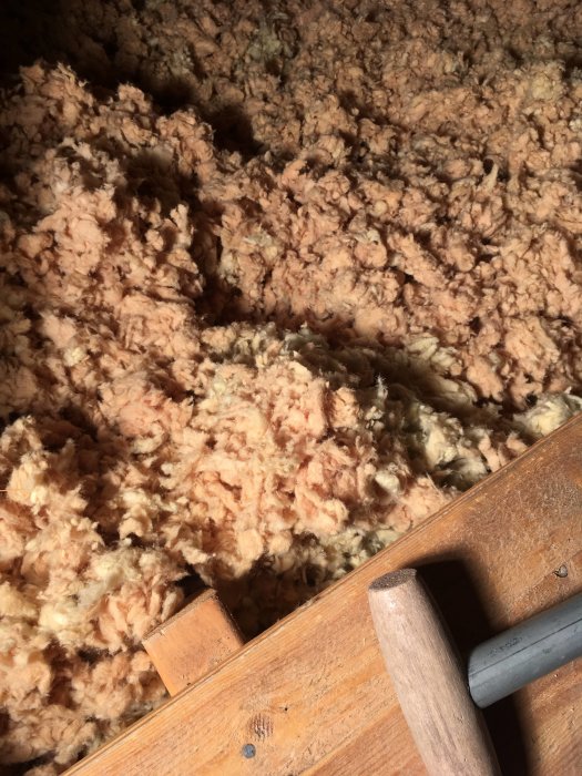 Vindisolering med lätt rosafärgad missfärgning ovanför badrum, närliggande isolering är normal färg, träbjälkar synliga.