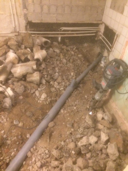 Nylagd avloppsrör i uppgrävd jord med stenar och gammal rörstapel i bakgrunden.