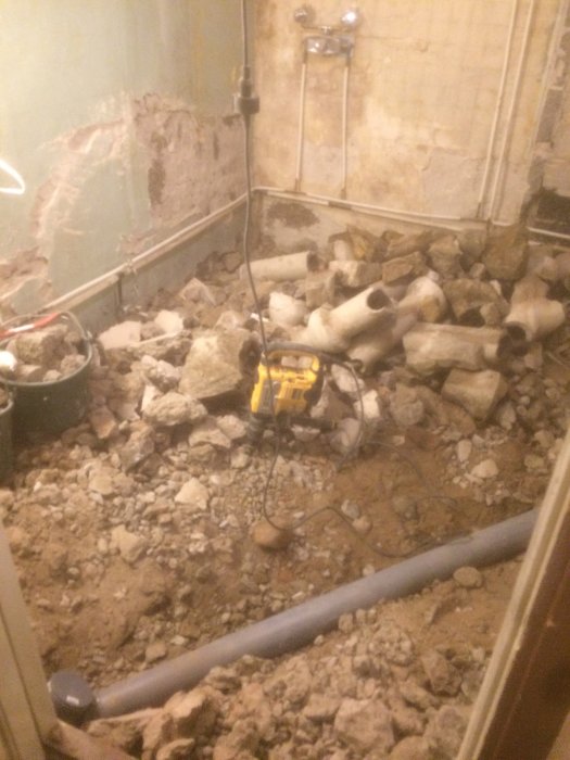 Rivningsarbete i badrum med grus, rör och borr i fokus.