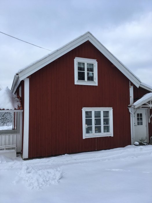 Röd stuga med snötäckt gavel under vintern som planeras för en utbyggnad.