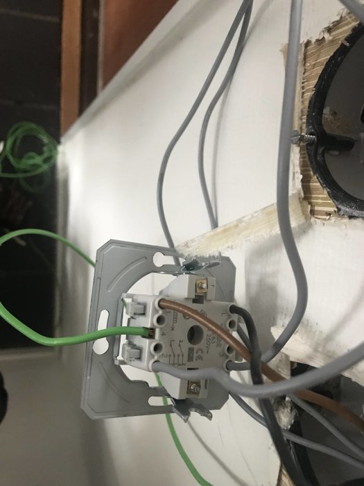 Oorganiserade elektriska kablar och en strömbrytare monterad på en vit vägg.