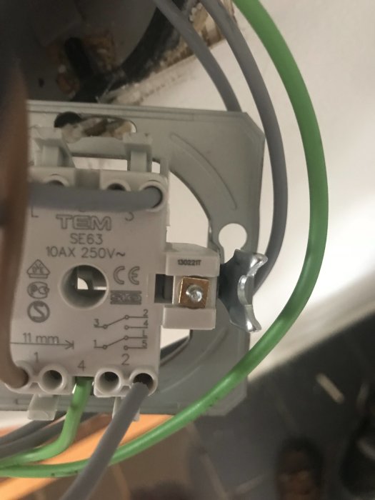 Närbild på en elektrisk anslutning på baksidan av en strömbrytare med gröna och grå kablar.