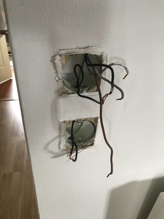 Två öppna elektriska dosor i en vägg med exponerade kablar och avskalad kabel runt en skruv.