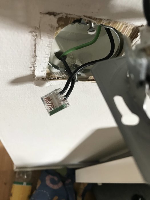 Öppen vägguttag med osammanlänkade gröna, svarta och bruna kablar samt ett löstaget RJ45-uttag.