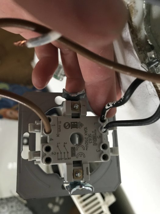 En hand som håller en elektrisk strömbrytare med synliga ledningar och anslutningar.