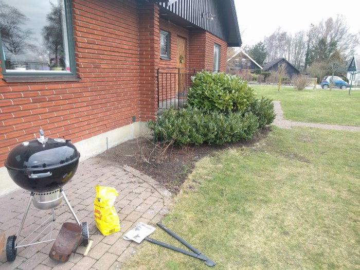 Renoverat trädgårdsland framför tegelhus, gräsmatta, grill och trädgårdsverktyg.