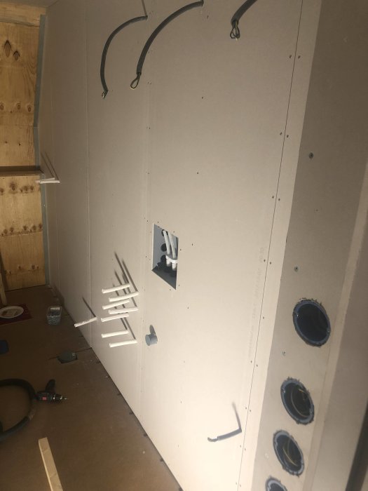 Gipsvägg med utskärningar för rör och elinstallationer i pågående badrumsrenovering.