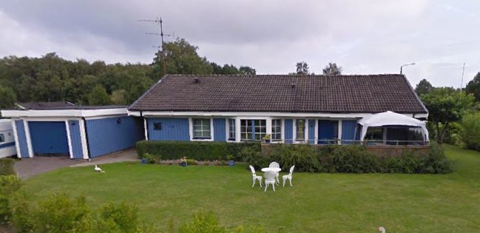 Ett blått enfamiljshus med en välhållen trädgård och vita trädgårdsmöbler framför huset.