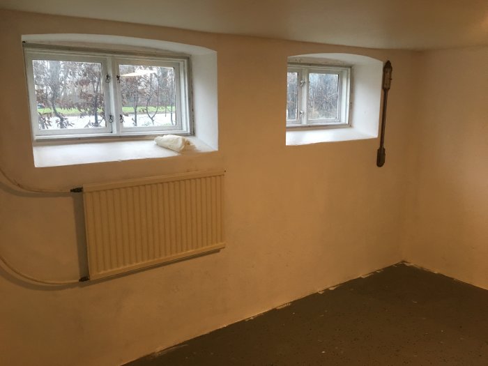 En källare under renovering med nymålade vitmålade väggar och två fönster med utsikt mot trädgården.