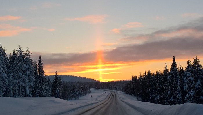 Vinterväg i Arjeplog med riklig snö och solnedgång med ljuspelar fenomen.