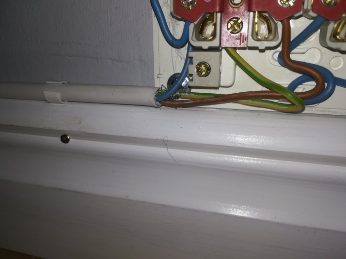 Eluttag med improviserad jordfläta på en skalad kabel, vid vit vägg och list.