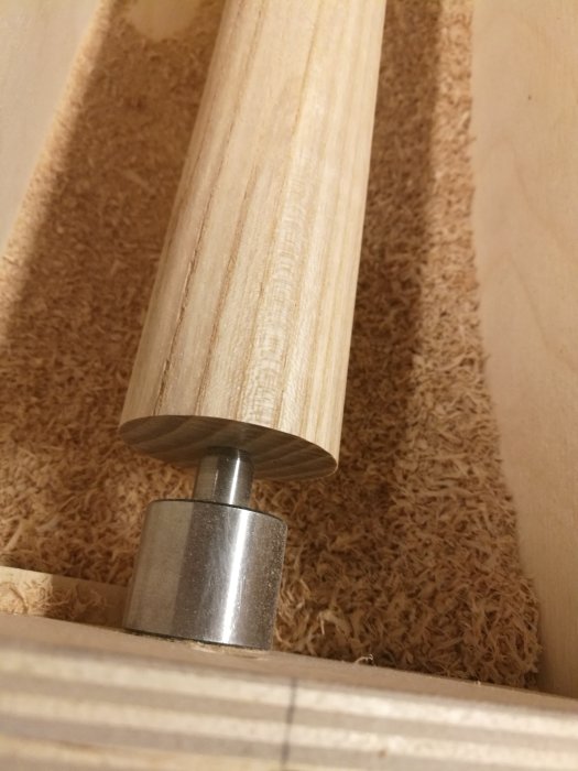 En rundstav i ek monterad i en hemmagjord träbearbetningsanordning med spånor i bakgrunden.