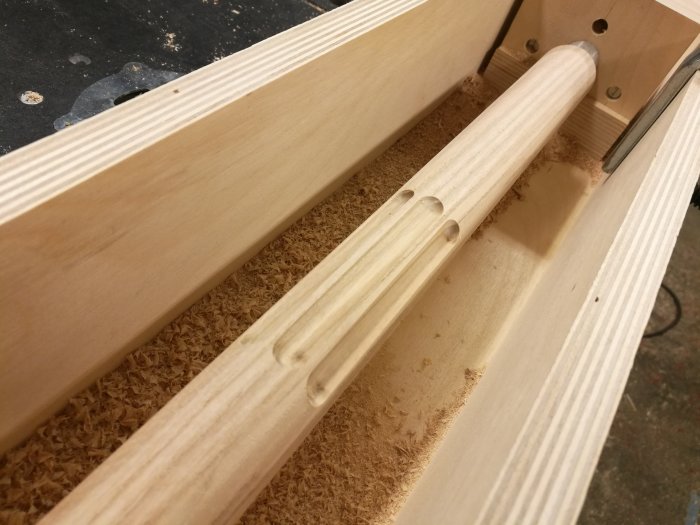 Fräst rundstav i ek med precisionsspår placerad i en hemmagjord svarvränna med spånor.