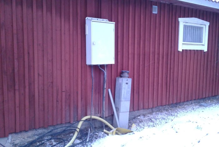 Elfordonsskåp och kabelskåp vid röd stallvägg med snö på marken.