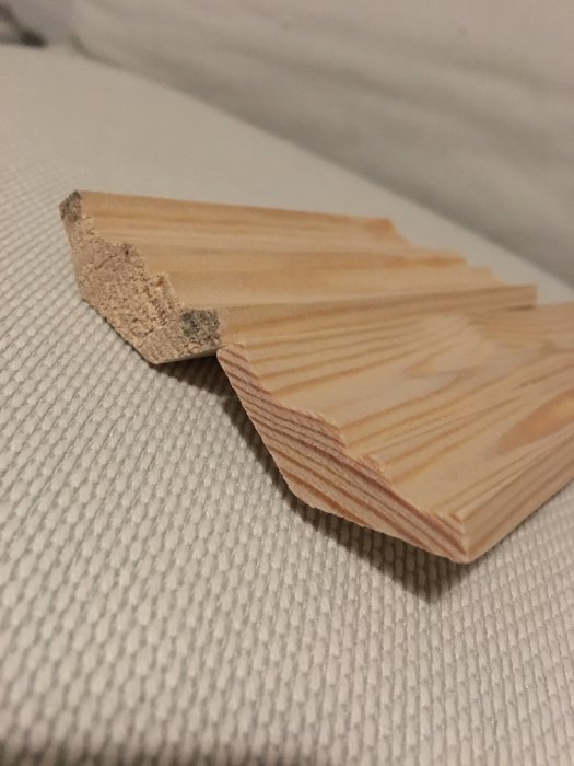 Två taklister i trä med olika skärningsvinklar på textilunderlag.