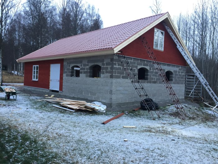 Nybyggt garage med lecaväggar och röda detaljer under vinter, material och stegar framför.