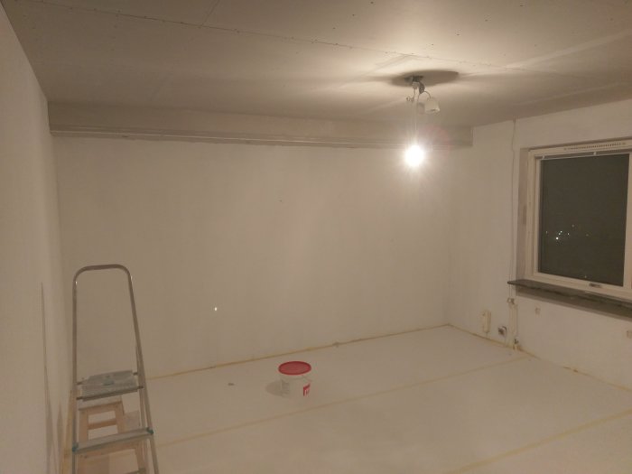 Rum under renovering med skyddad golv, hörnskydd på takboxar klara för målning, och en stege.