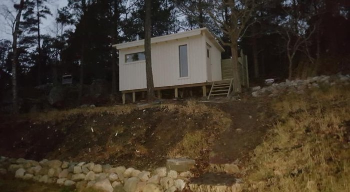 Fristående vedeldad bastu under uppförande, belägen på en sluttning utanför en skog.