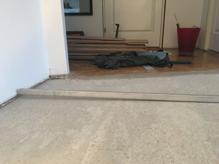 Ojämn betonggolv med en synlig höjdskillnad nära en vägg, omgiven av byggmaterial.