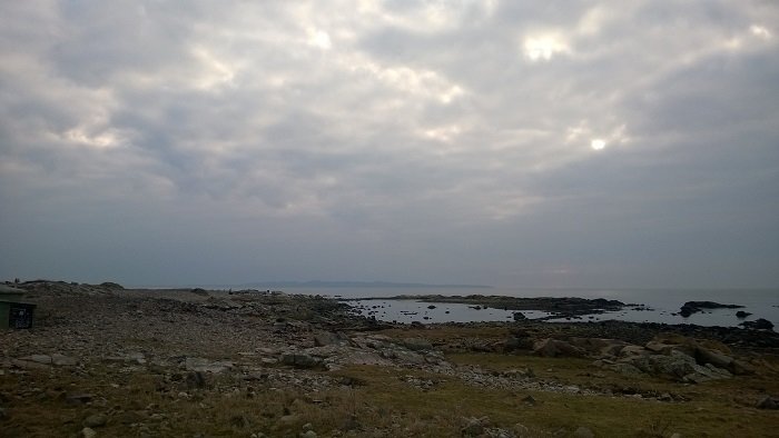 Kustlandskap i Skåne med molnigt himmel och hav i bakgrunden.